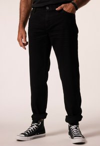 Černé džíny z denimu s volným střihem, ohrnutými manžetami a předními kapsami, v kombinaci s černými vysokými teniskami s bílou podrážkou.