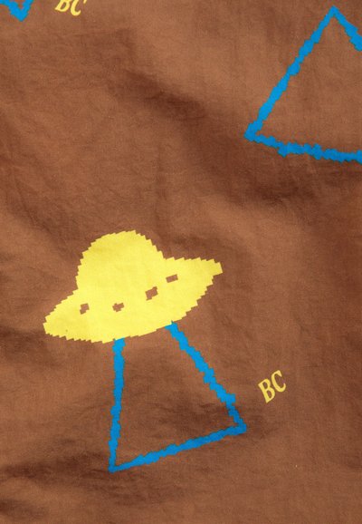 OVNI jaune avec un rayon triangulaire pixelisé bleu et les lettres BC sur un fond en tissu marron.