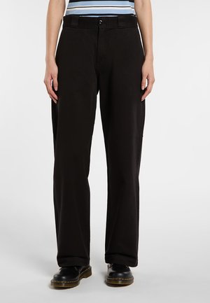 Persona che indossa pantaloni neri a gamba dritta, scarpe nere con lacci e una vista tronca di una camicia a righe.