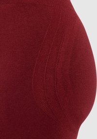 Rode gebreide stof met een gladde textuur, een gecontourde vorm en intrigerende ribbeldetails langs de zijkant.