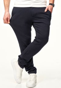 Navyblaue Jogginghosen aus weichem Stoff, mit Seitentaschen und schmalem Schnitt, kombiniert mit weißen Sneakers. Die Textur wirkt glatt.