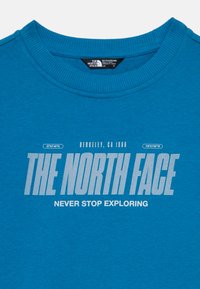 Felpa in cotone blu con collo a coste. Presenta il logo "THE NORTH FACE" e la scritta "NEVER STOP EXPLORING" in bianco. Etichetta della taglia visibile.
