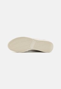 Shoe sole with a rubber material, light beige color, featuring an embossed logo and a zigzag pattern for traction.