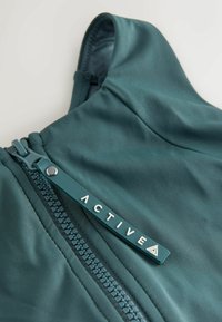 Blågrøn hættetrøje med glat tekstur, frontlynlås og et logo-mærke præget med "ACTIVE". Stoffet har en subtil glans.
