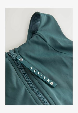 Jaket s kapuljačom tirkizne boje, glatke teksture, s prednjim patentnim zatvaračem i oznakom s logotipom utisnutim s natpisom "ACTIVE." Tkanina ima suptilni sjaj.