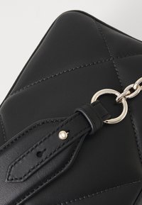 Svart handväska i konstläder med quiltat mönster och blankt silverfärgat hardware. Utrustad med avtagbar rem och en ringfäste.