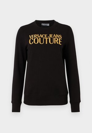 Melna sporta krekls ar ribinātu piedurkņu un apakšmalu, ar izteiksmīgu zeltītu izšuvumu "VERSACE JEANS COUTURE" tekstu uz priekšpuses.