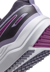 Gros plan sur le talon d'une chaussure de course violette et blanche avec une semelle texturée et une étiquette "RUNNING" sur un panneau noir.