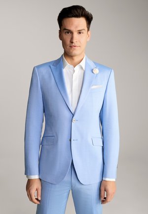 Helles blaues Anzug aus strukturiertem Stoff, mit einem geschlitzten Revers, doppelten Taschen, weißem Hemd und einer floralen Anstecknadel als Akzent.