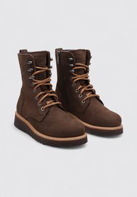Botas de cuero marrón con cordones y herrajes plateados, cuello acolchado y cremallera lateral. Suela de goma gruesa con borde cosido para mayor durabilidad.