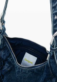 Denim válltáska cipzáras tetejével. A belső rész sötét béléssel és "Desigual" feliratú címkével rendelkezik. Díszített virágminták találhatóak rajta.