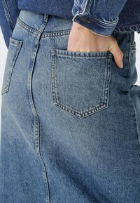 Svetlo modra jeans kratka krila z visokim pasom, ki ima pet žepov in vidne šive. Tekstura je nekoliko obrabljena.