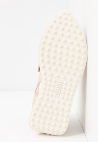 Semelle de basket en caoutchouc blanc avec grip texturé, dotée d'une tige rose clair avec des accents en daim. Logo embossé près du talon.