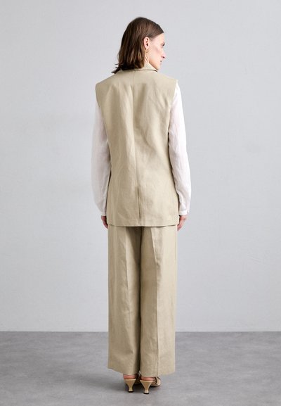 Gilet en lin beige avec une coupe ajustée, associé à un pantalon large assorti. Texture lisse, design minimaliste et silhouette épurée.
