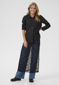 Black button-up shirt with long sleeves and a dressy design, paired with a sheer navy lace maxi skirt over denim flared pants.