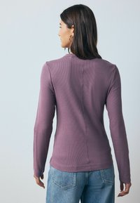 Long-sleeve top in soft mauve ribbed fabric, featuring a round neckline and back seam detail, paired with light blue denim jeans.