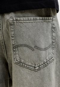 Gesäßtasche einer ausgewaschenen grauen Jeans, getragen mit schwarzem Hemd, zeigt die Nahtdetails und den Stofftextur.