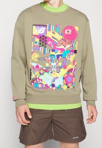 Olivgrön tröja med en livlig, flerfärgad grafisk design med abstrakta former och mönster. Ribbad muddar och rundad halsringning.