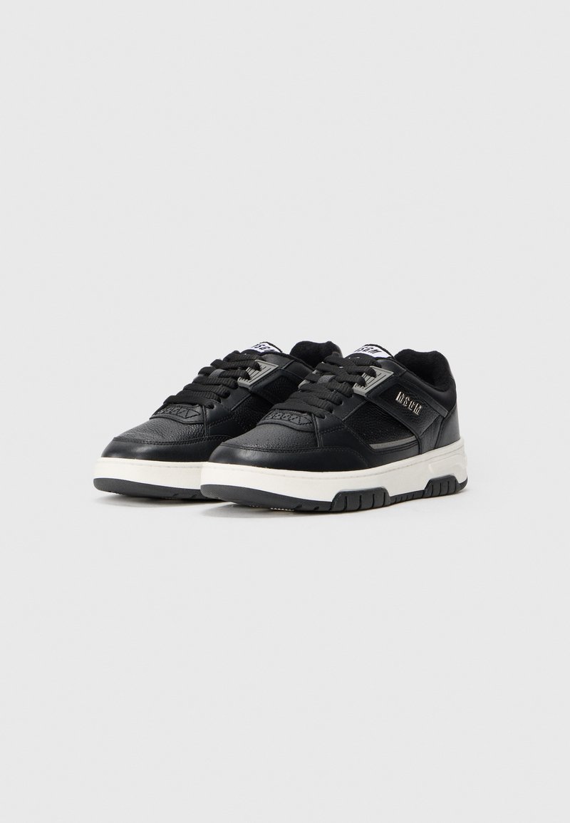 Schwarze Sneaker mit einem strukturierten Lederoberteil, weißer Gummisohle, gepolstertem Schaftrand und schwarzen Schnürsenkeln. Mit einem Markenakzent an der Seite.