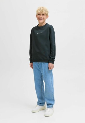 Sweatshirt vert foncé avec col rond, logo brodé sur la poitrine, associé à un jean bleu clair à coupe décontractée et des baskets blanches.