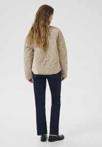 Beige quilted jacket with a textured pattern and a relaxed fit, paired with dark blue straight-leg jeans and black shoes.