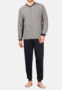 Graues Langarmoberteil mit V-Ausschnitt und einer Brusttasche; marineblaue Hose mit elastischen Bündchen. Das Outfit besteht aus weichem, strukturiertem Stoff.