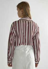 Camisa de manga larga a rayas verticales en granate y blanco, con un cuello clásico y puños abotonados, combinada con pantalones blancos de cintura alta.