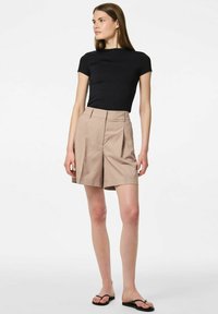 Haut noir à manches courtes associé à un short beige plissé. Le short a une coupe ample et est fabriqué dans un tissu lisse et léger. Tongs noires.