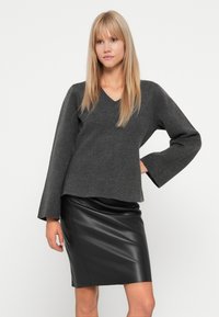 Maglione grigio in misto lana con scollo a V e maniche a campana, abbinato a una gonna in pelle nera aderente, texture liscia e finitura lucida.