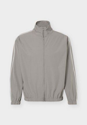 Veste de survêtement gris clair zippée avec col montant, poignets élastiques, ourlet et fines rayures blanches courant sur toute la longueur des manches.