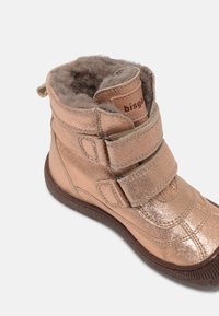 Botte d’hiver enfant rose métallisée avec double fermeture Velcro et doublure en polaire douce, présentée en angle sur fond blanc.