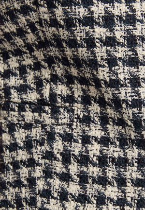 Un tessuto intrecciato presenta un motivo a pied de poule in blu navy scuro e bianco, evidenziando una superficie testurizzata con fili sfilacciati per un effetto visivo interessante.