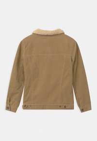 Hnědá kordová bunda s kožešinovým límcem, dlouhými rukávy a patentkami na manžetách. Má vertikální žebrovanou strukturu.