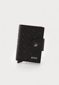 Black wallet made of textured material, featuring a snap closure, embossed pattern, and silver logo detail on the lower right.