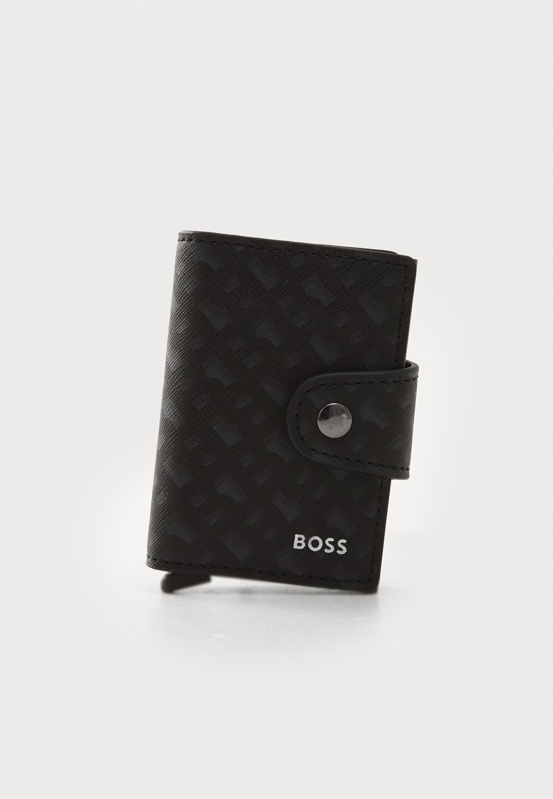 Black wallet made of textured material, featuring a snap closure, embossed pattern, and silver logo detail on the lower right.