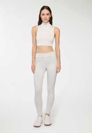 Top corto bianco senza maniche con colletto alto abbinato a leggings aderenti grigio chiaro. Outfit realizzato in tessuto elastico, dalla texture liscia e dal design semplice.