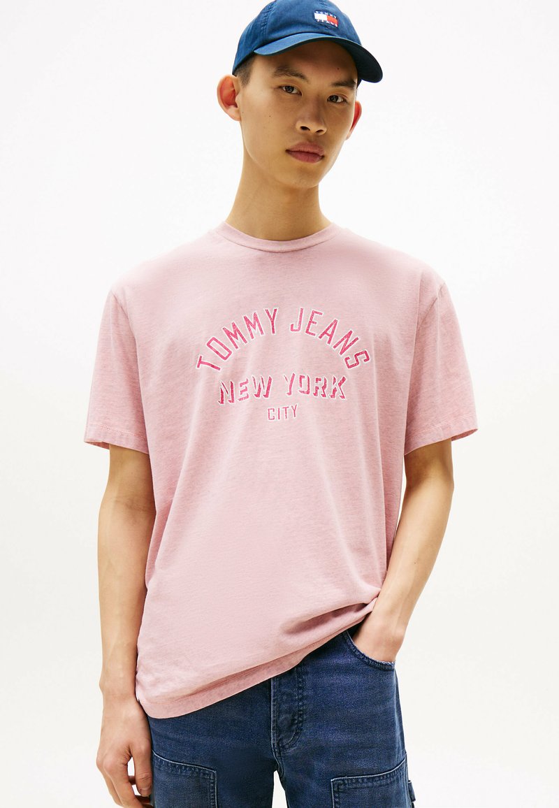 Lichtroze T-shirt met korte mouwen, ronde hals en een gestructureerde stof. Voorzien van het logo "TOMMY JEANS NEW YORK CITY" in contrasterende kleuren.