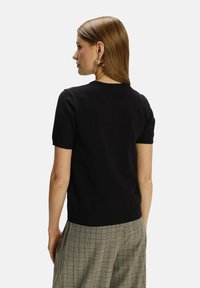 Maglione nero a maniche corte con scollo rotondo, in maglia liscia. Abbinato a pantaloni a quadri beige, con una vestibilità sartoriale.