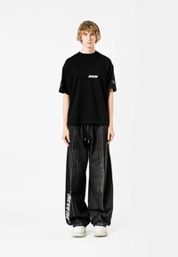 Camiseta negra con el logo blanco "MWM", combinada con pantalones de mezclilla negros holgados que presentan un diseño de franjas laterales y una cintura elástica.
