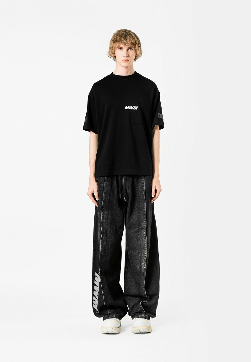 Camiseta negra con el logo blanco "MWM", combinada con pantalones de mezclilla negros holgados que presentan un diseño de franjas laterales y una cintura elástica.
