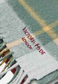 Sciarpa di lana a quadri in verde, bianco e giallo, con bordi frangiati. Presenta un ricamo con la scritta "VICTORIA HYDE LONDON." Superficie morbida e testurizzata.