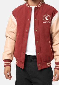 Czerwona kurtka varsity z mieszanki wełny z beżowymi skórzanymi rękawami, prążkowanymi ściągaczami w paski i haftowanym na piersi logo „KARL KANI”.