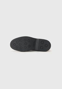 Suola di scarpa in gomma nera con battistrada circolare e superficie liscia. "Calvin Klein" stampato vicino al tallone. Design minimalista.