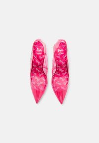 Talons hauts transparents roses avec un bout pointu et une semelle intérieure à motif de logo Barbie. Caractéristiques d'une fine sangle de cheville et d'une finition brillante.