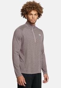 Grå, langærmet atletisk zip-up skjorte med høj krave, der har subtile striber og et logo på brystet. Blødt, let materiale.