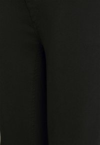 Svart denimtyg med en mjuk textur, subtila sömnadsdetaljer och en åtsittande design. Närbild som framhäver sid söm.