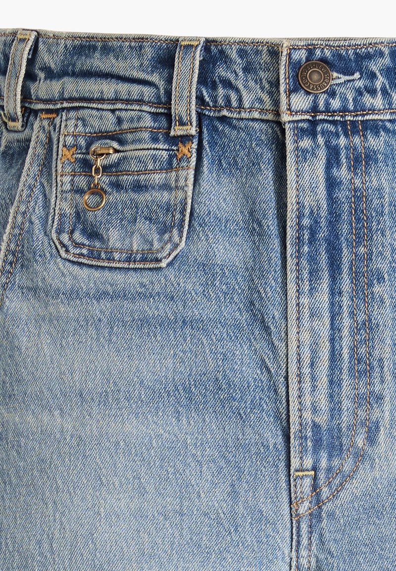 Gros plan d’un jean en denim bleu clair avec poche avant, bouton en métal, passants de ceinture et un petit porte-clés en métal attaché à la fermeture éclair de la poche à monnaie.