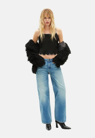 Schwarzes kurzes Oberteil mit gewelltem Saum und Perlenakzenten, kombiniert mit hellblauen, weit geschnittenen Jeans und schwarzen, spitz zulaufenden Stiefeln mit Absatz. Strukturierte, schwarze Oberbekleidung.