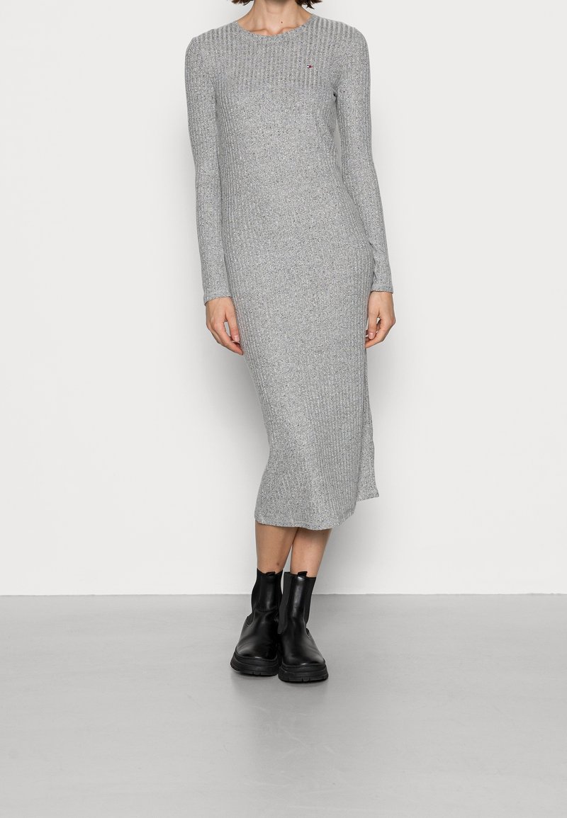 Robe longue en maille côtelée grise, manches longues, longueur au genou, avec un col rond et des fentes latérales. Assortie à des bottines noires.