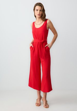 Combinaison sans manches rouge avec un buste ajusté et des jambes larges, dotée d'une ceinture à nouer et de poches latérales. Tissu lisse de couleur unie.